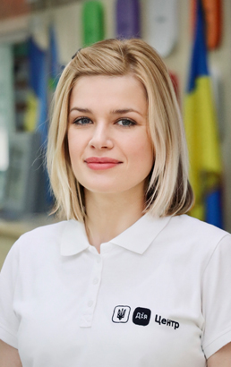 Жінка зі світлим каре, у білій футболці з логотипом.